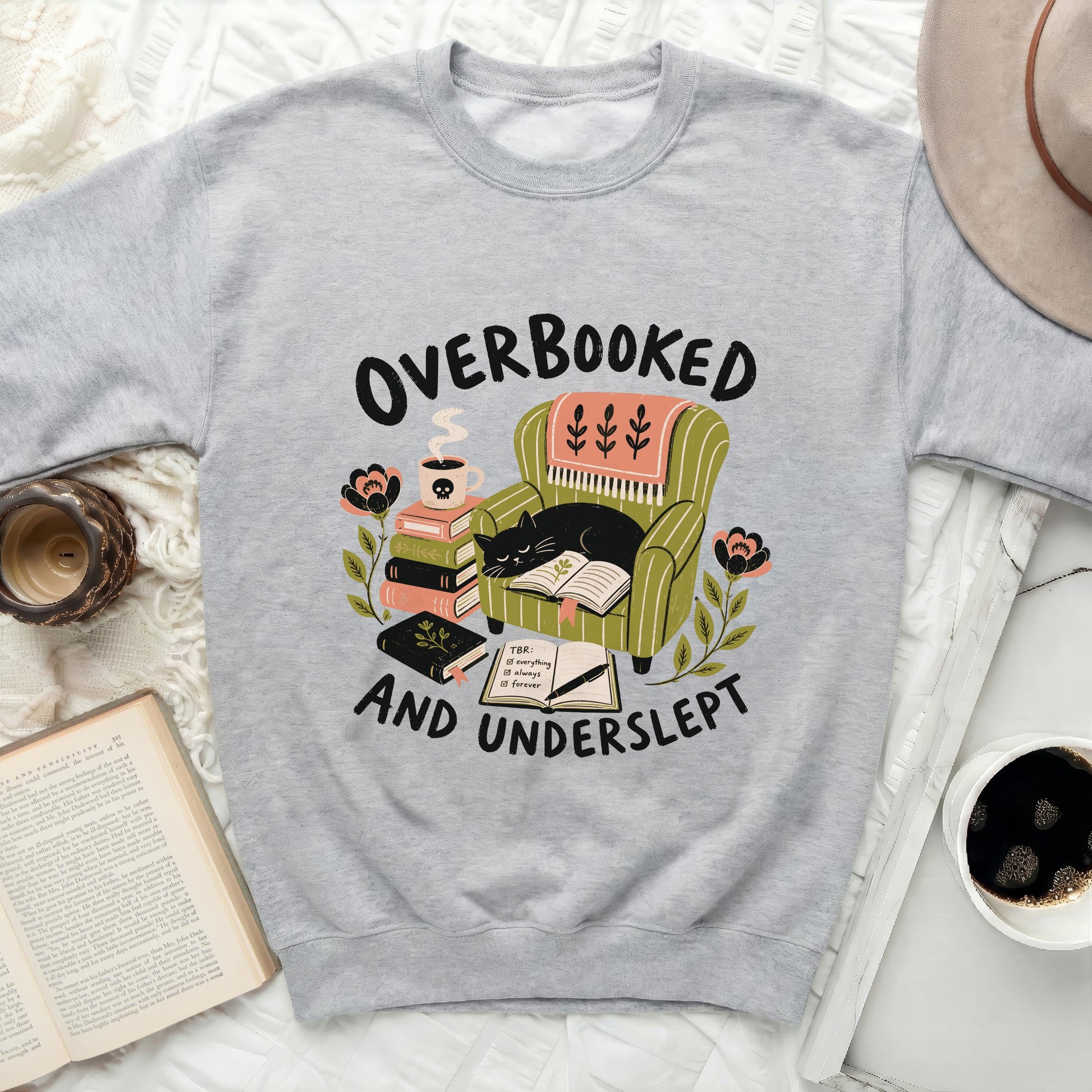 Light gray sweatshirt with "Overbooked and Underslept" graphic of a cat reading in a chair.