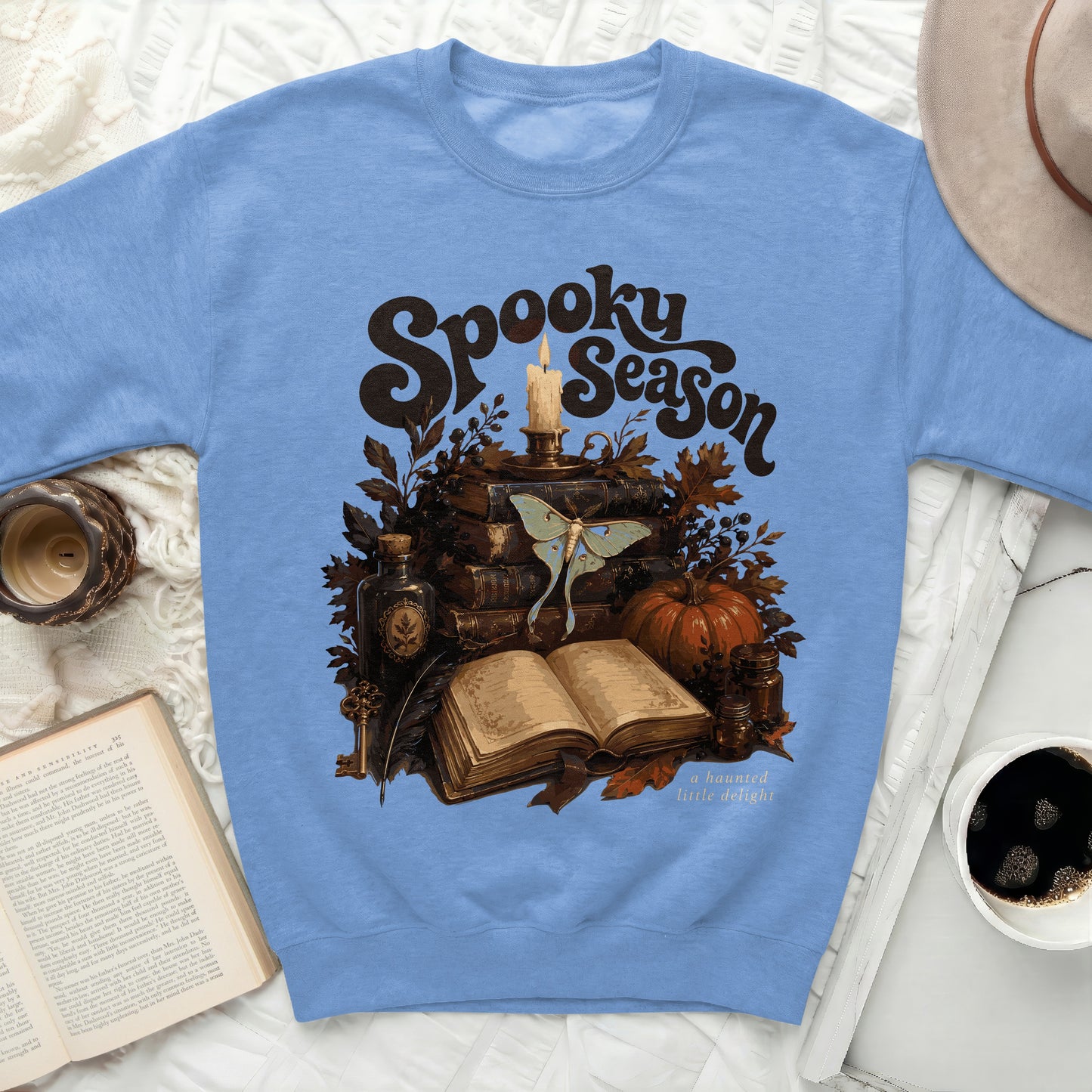 Blue sweatshirt with "Spooky Season" graphic featuring books, moth, candle, and pumpkin.