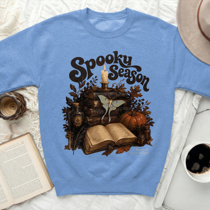 Blue sweatshirt with "Spooky Season" graphic featuring books, moth, candle, and pumpkin.