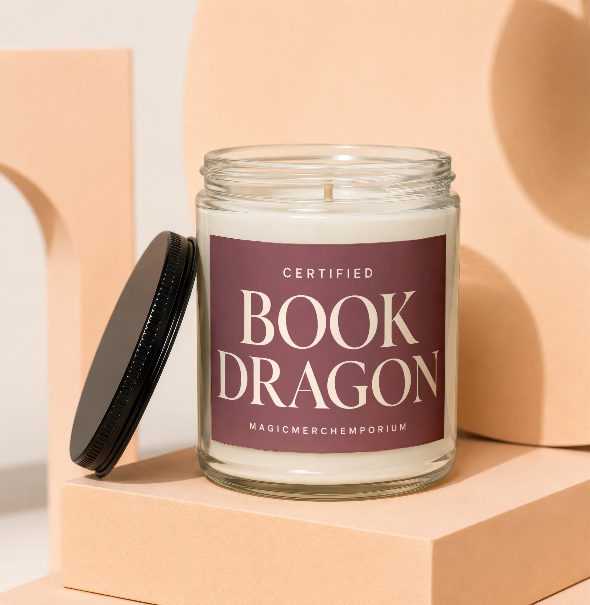 Glass candle with "Book Dragon" text and black lid on display blocks.
