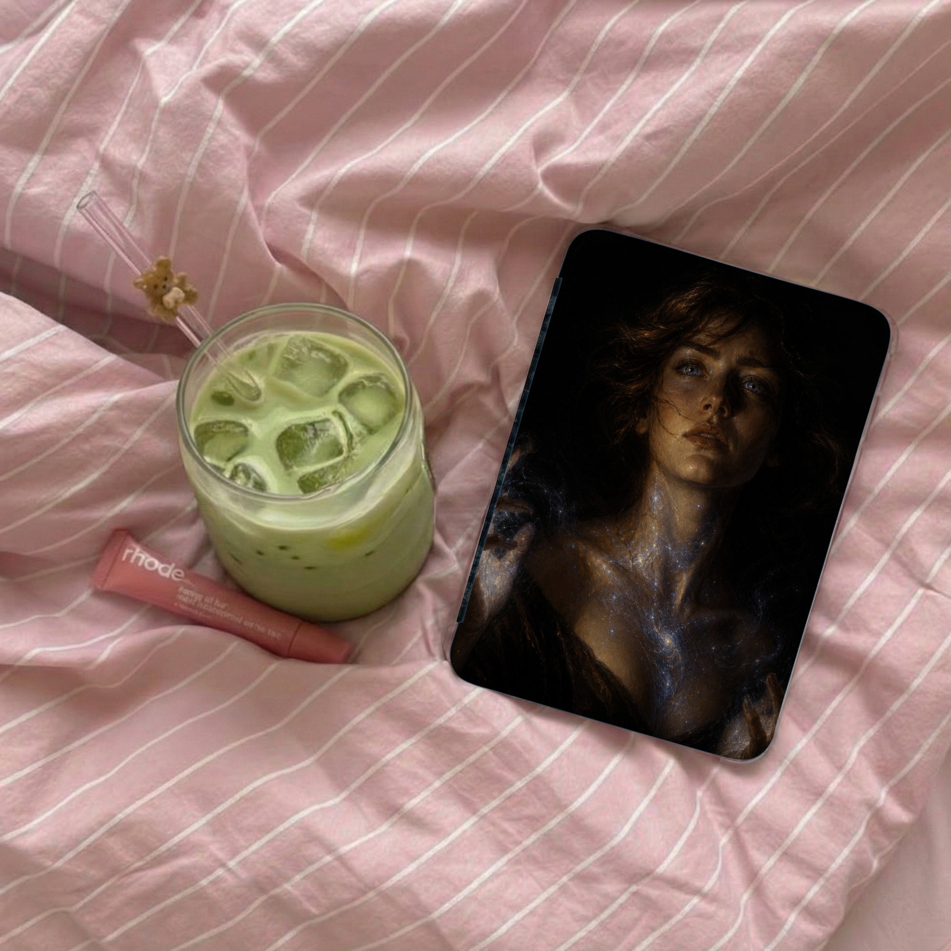 Glass of green matcha drink with ice next to a Rhode lip balm and a phone case.