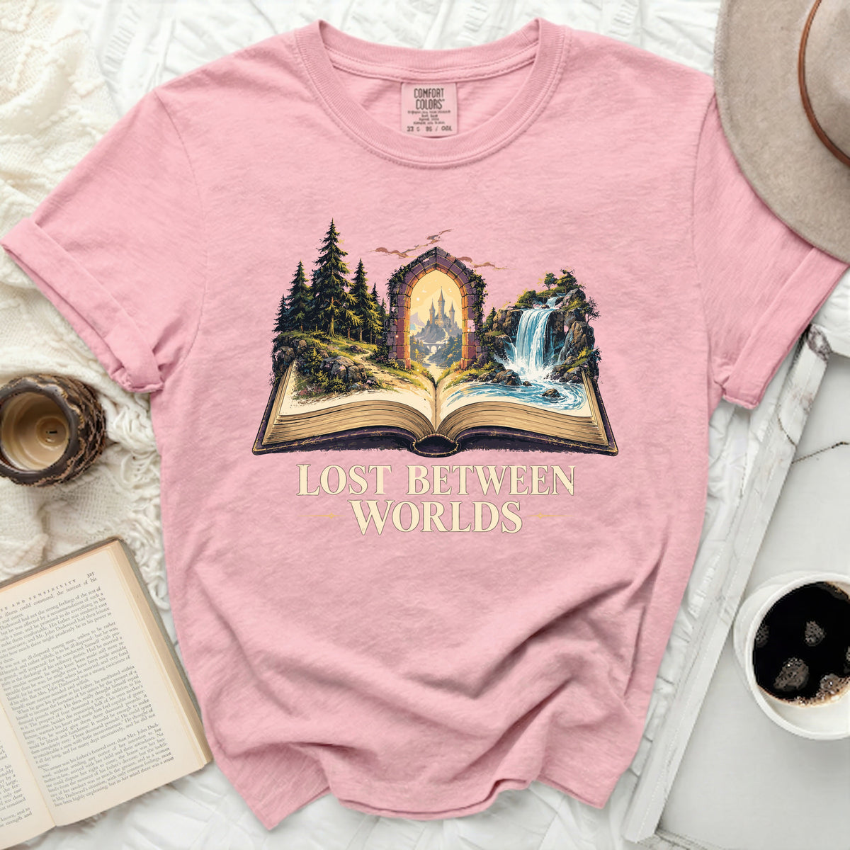 Pink t-shirt with "Lost Between Worlds" text and open book fantasy art.