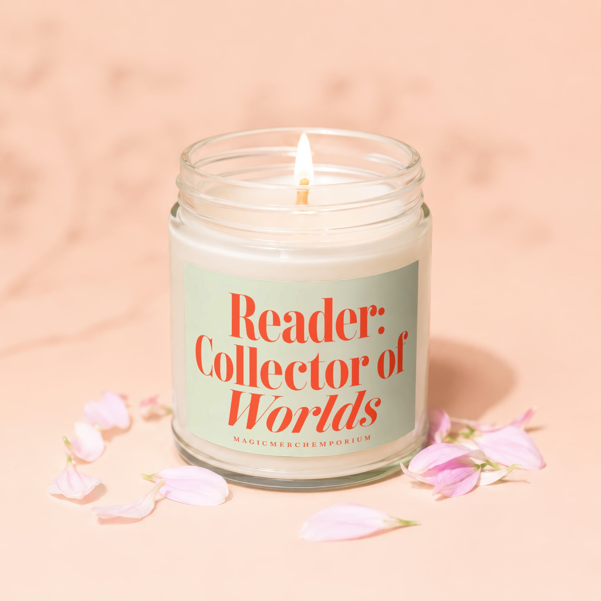 Lit glass jar candle with a light-colored label reading "Reader: Collector of Worlds"