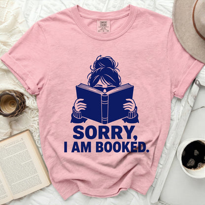 Pink t-shirt with dark blue graphic of a woman reading and text "SORRY, I AM BOOKED."