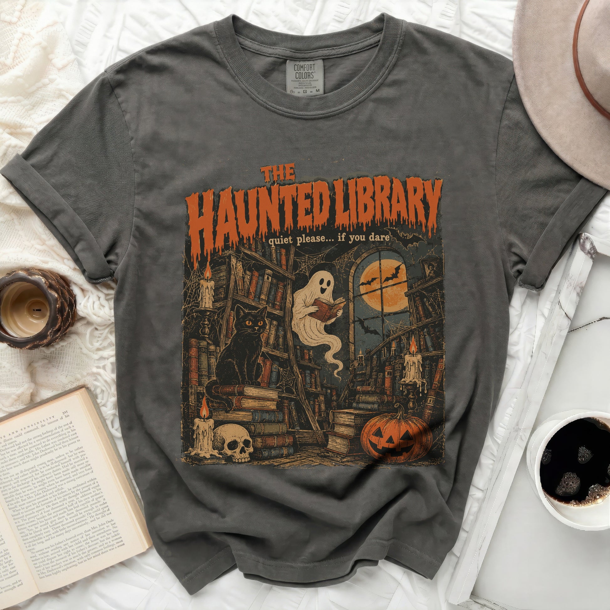 The Haunted Library graphic tee features books, a black cat, ghost, pumpkin, and moon.