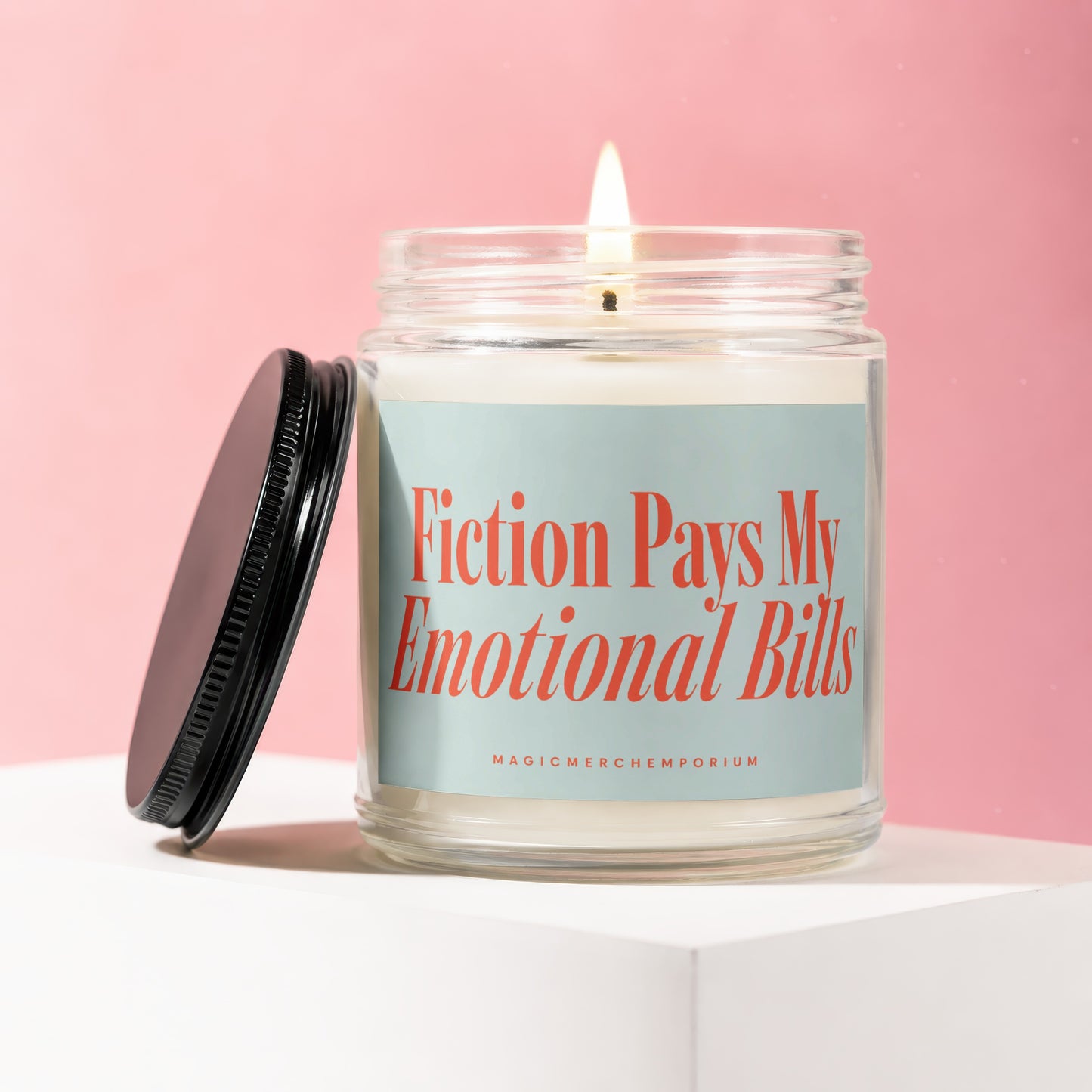 Candle with "Fiction Pays My Emotional Bills" text in a glass jar with lid off.