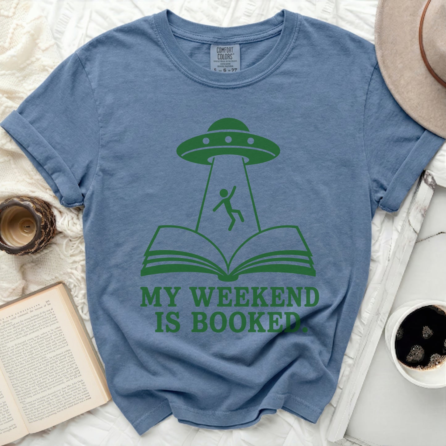 Blue t-shirt with green alien abduction over an open book graphic and text "MY WEEKEND IS BOOKED".