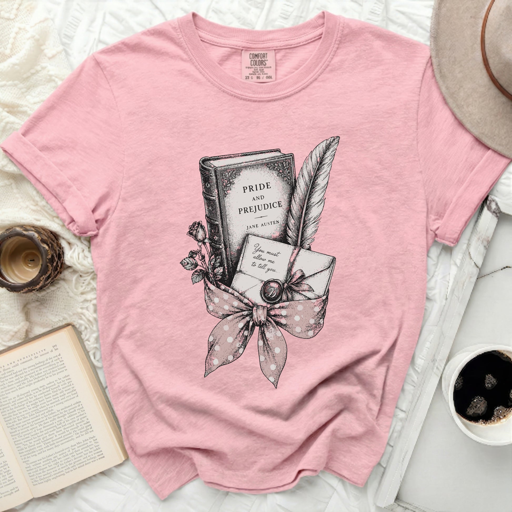 Pink t-shirt with "Pride and Prejudice" book, quill, letter, and rose graphic.