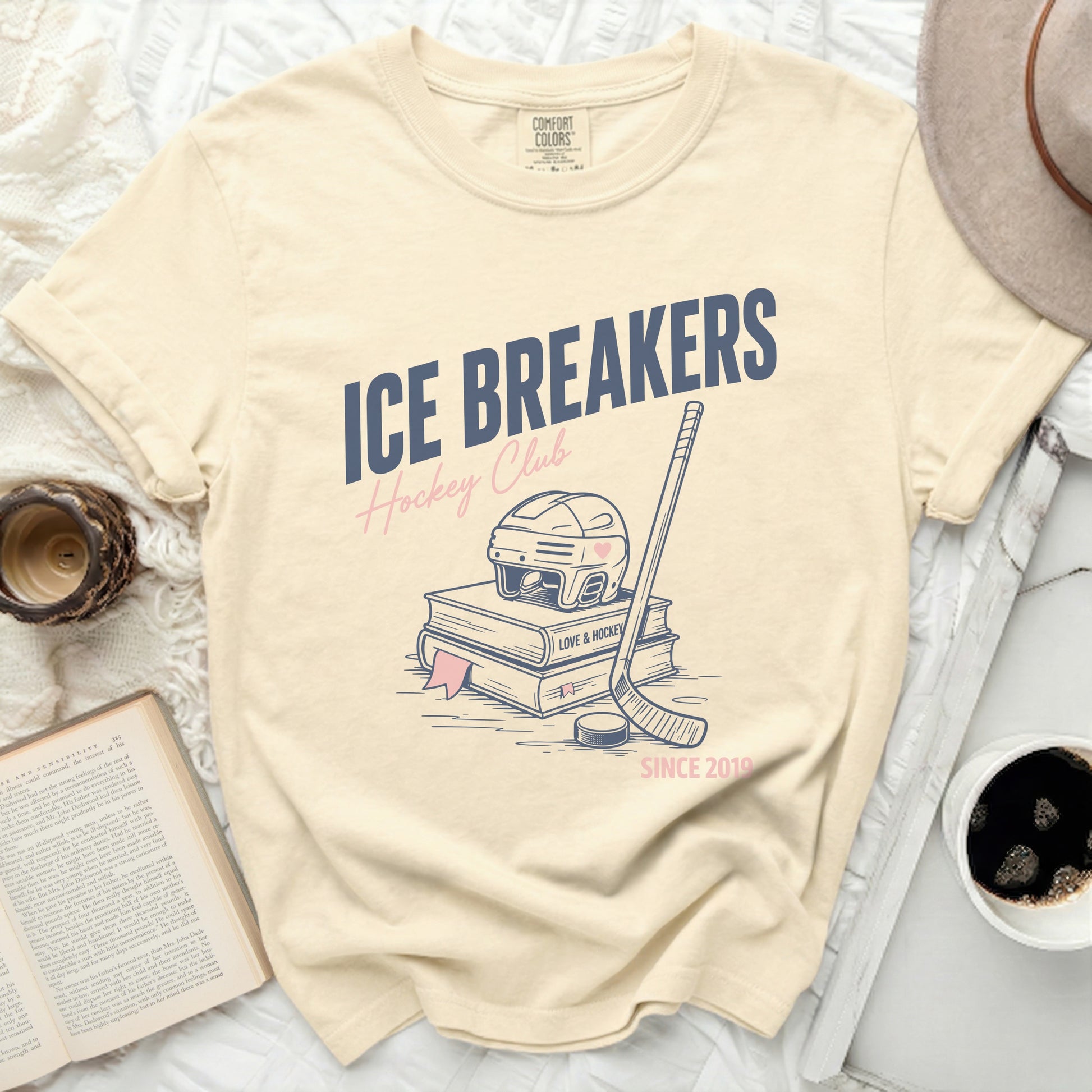 "ICE BREAKERS Hockey Club" text on a cream t-shirt with hockey stick and books.