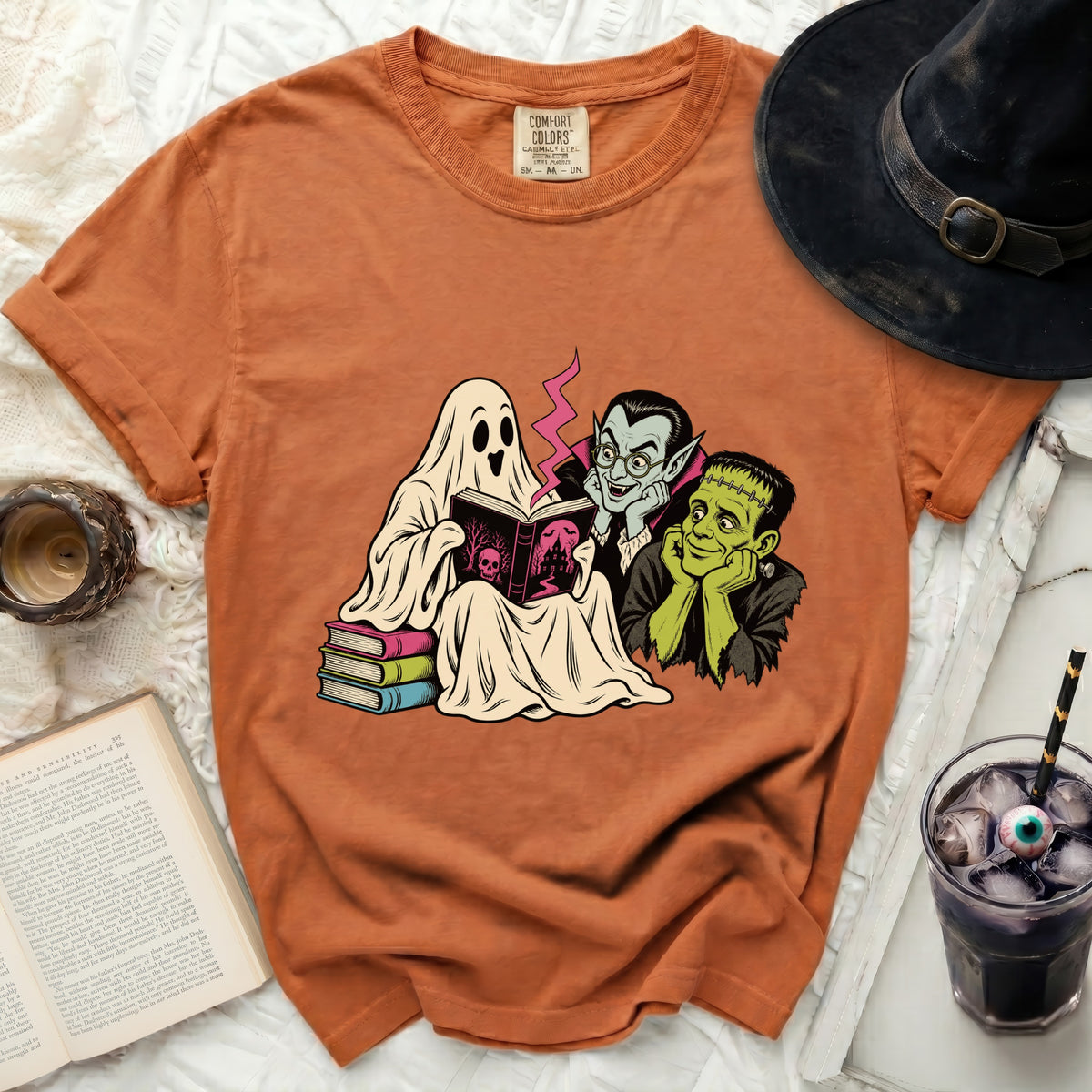 Ghost, vampire, and Frankenstein reading a book with a witch hat nearby.