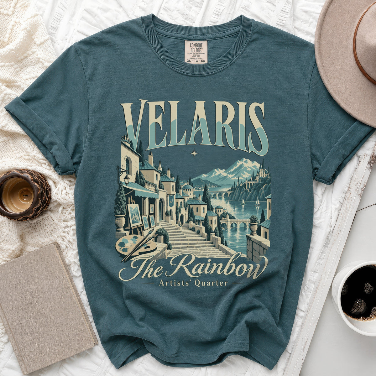 Teal t-shirt with Velaris Artists Quarter graphic, featuring a coastal town scene.