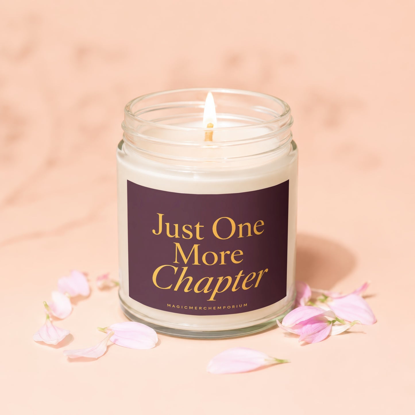 Glass candle with lit wick and label that reads "Just One More Chapter".