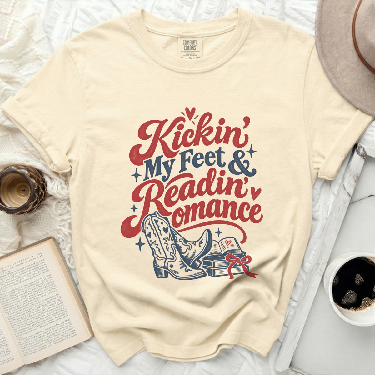 Cream t-shirt with "Kickin' My Feet & Readin' Romance" text, boots, and books.