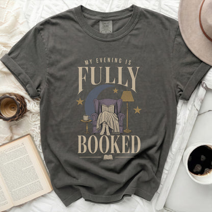 Graphic tee with "My Evening is Fully Booked" text and reading-themed illustration.