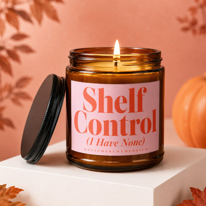 Lit amber glass candle with pink label reading "Shelf Control (I Have None)".