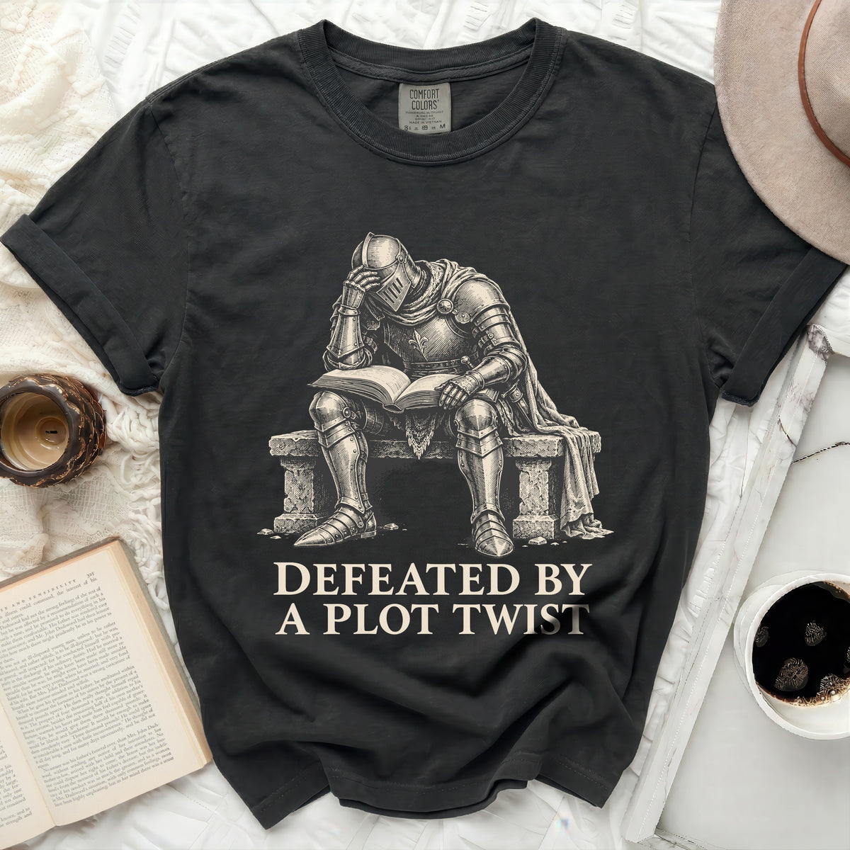 T-shirt with knight reading a book, text reads "Defeated by a plot twist."