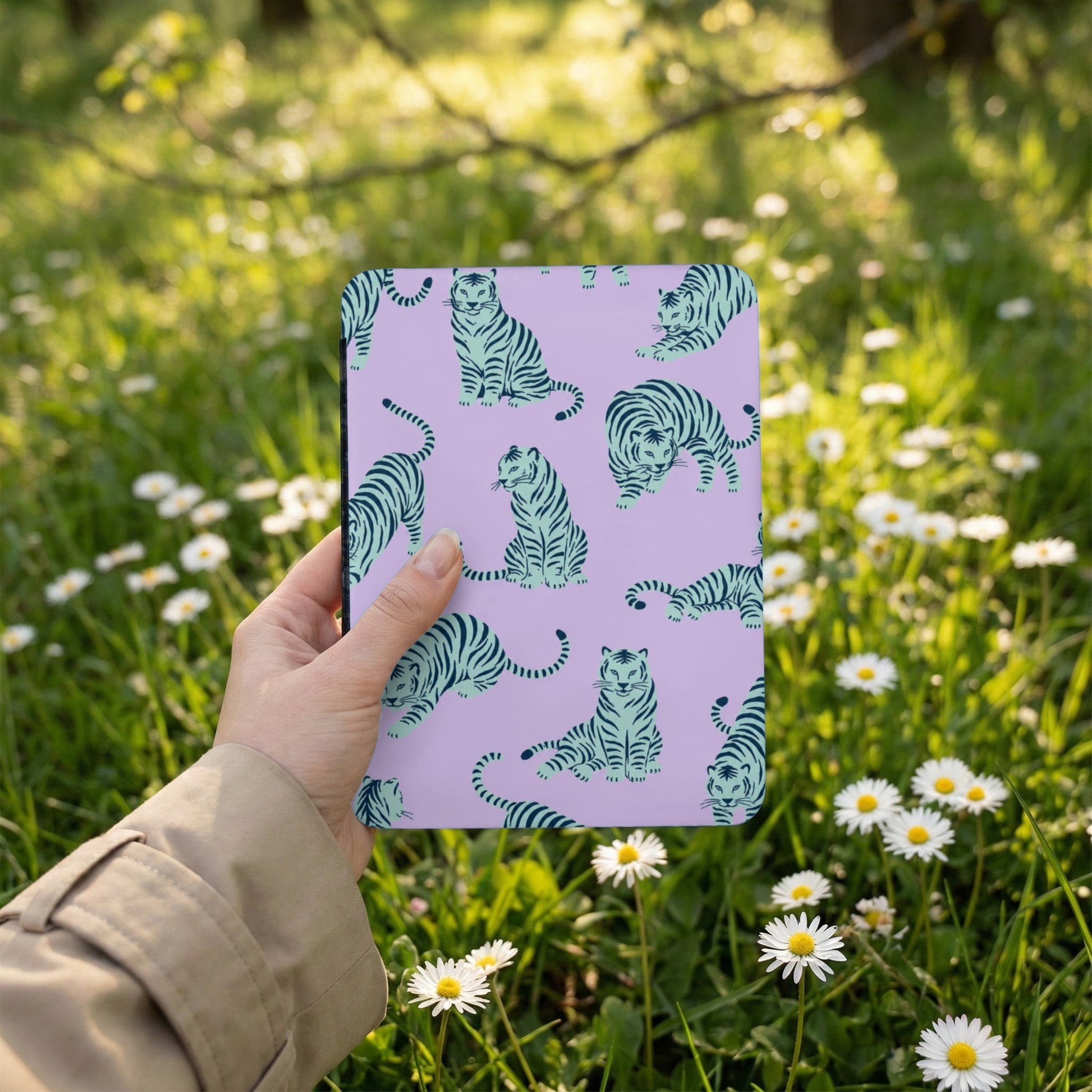 Notebook with repeating light blue tiger pattern on a lavender background, held outdoors.