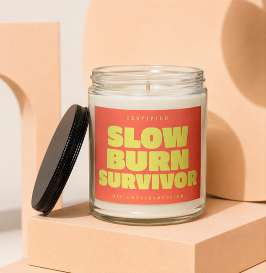 Glass jar candle with red label that says "CERTIFIED SLOW BURN SURVIVOR"