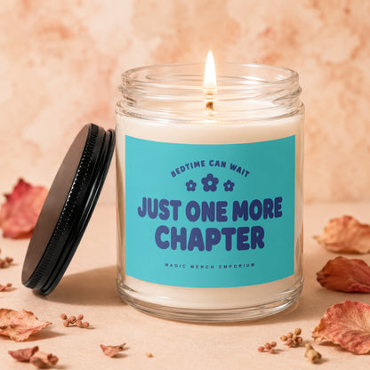 Glass jar candle with lit wick and blue label reading "Just One More Chapter".