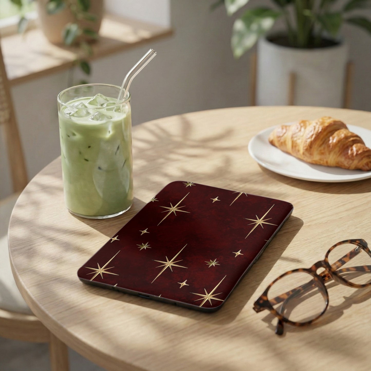 Maroon case with gold starburst pattern, next to a drink and croissant.