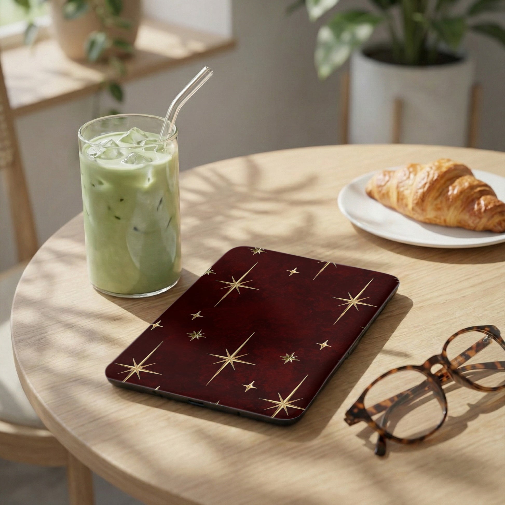 Maroon case with gold starburst pattern, next to a drink and croissant.