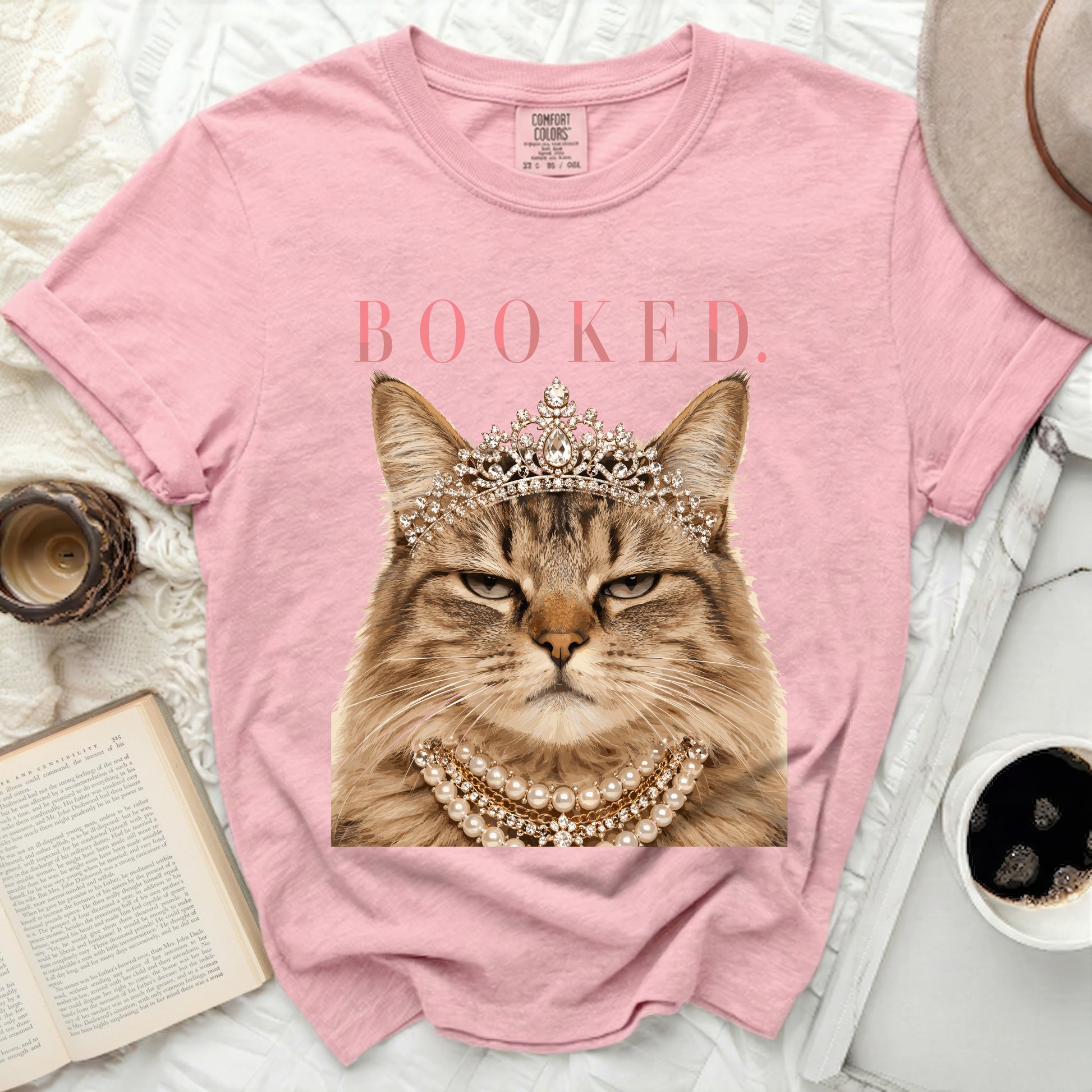 Pink t-shirt with a regal cat wearing a crown and pearl necklace, text "BOOKED."