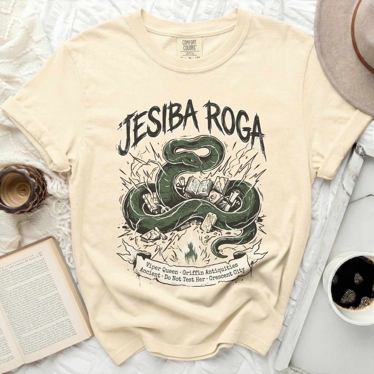 Cream t-shirt with green snake and books graphic, "Jesiba Roga" text.