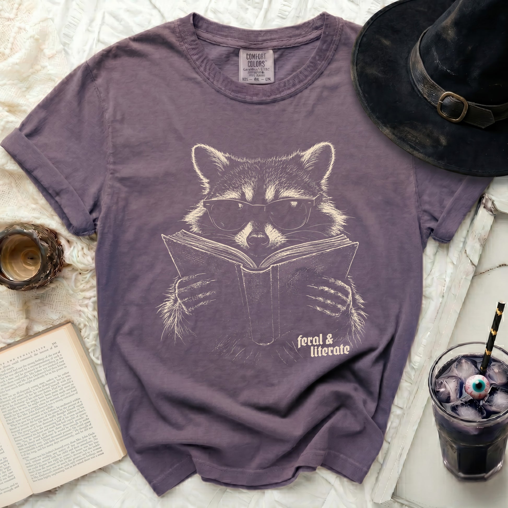 T-shirt with a raccoon wearing sunglasses reading a book.