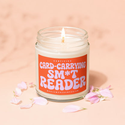 Burning candle with orange label that reads "Certified Card-Carrying S*** Reader".