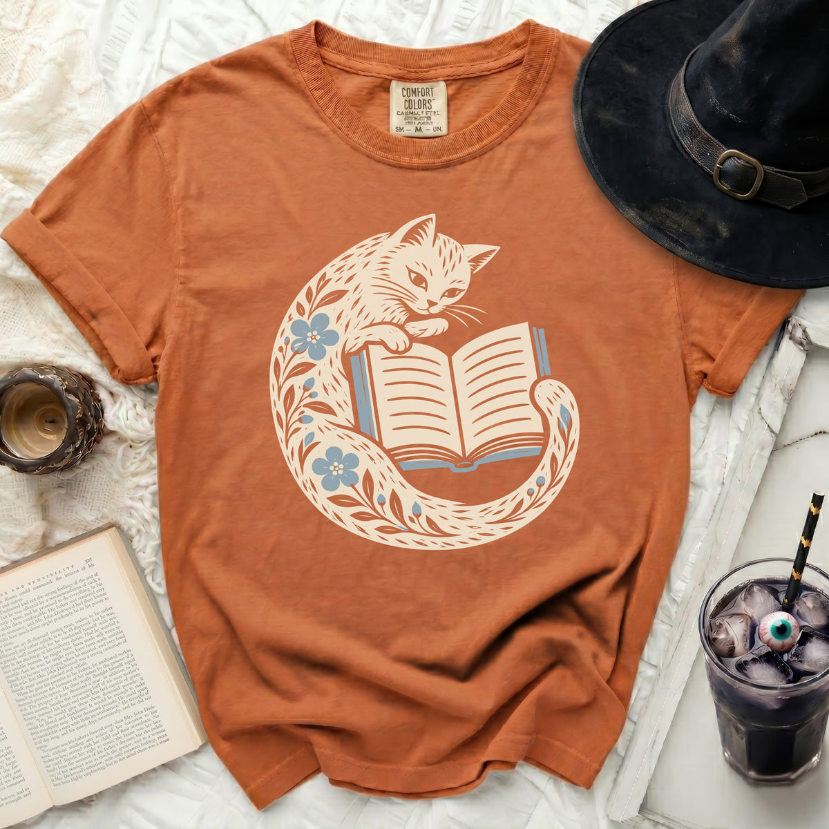 Orange t-shirt with a cream cat reading a book and floral design.
