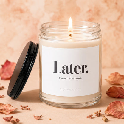 Glass candle with lit wick, black lid, and label reading "Later. I'm at a good part."