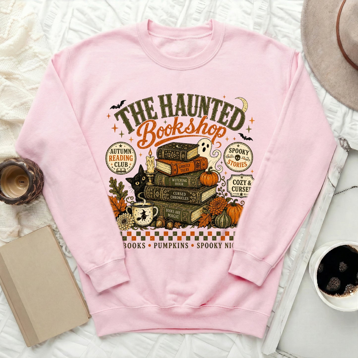 Pink sweatshirt with "The Haunted Bookshop" graphic featuring books, ghost, cat, and pumpkins.