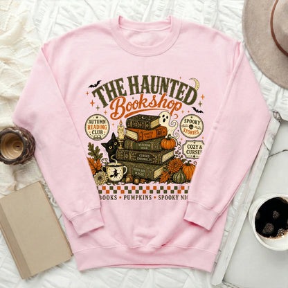 Pink sweatshirt with "The Haunted Bookshop" graphic featuring books, ghost, cat, and pumpkins.