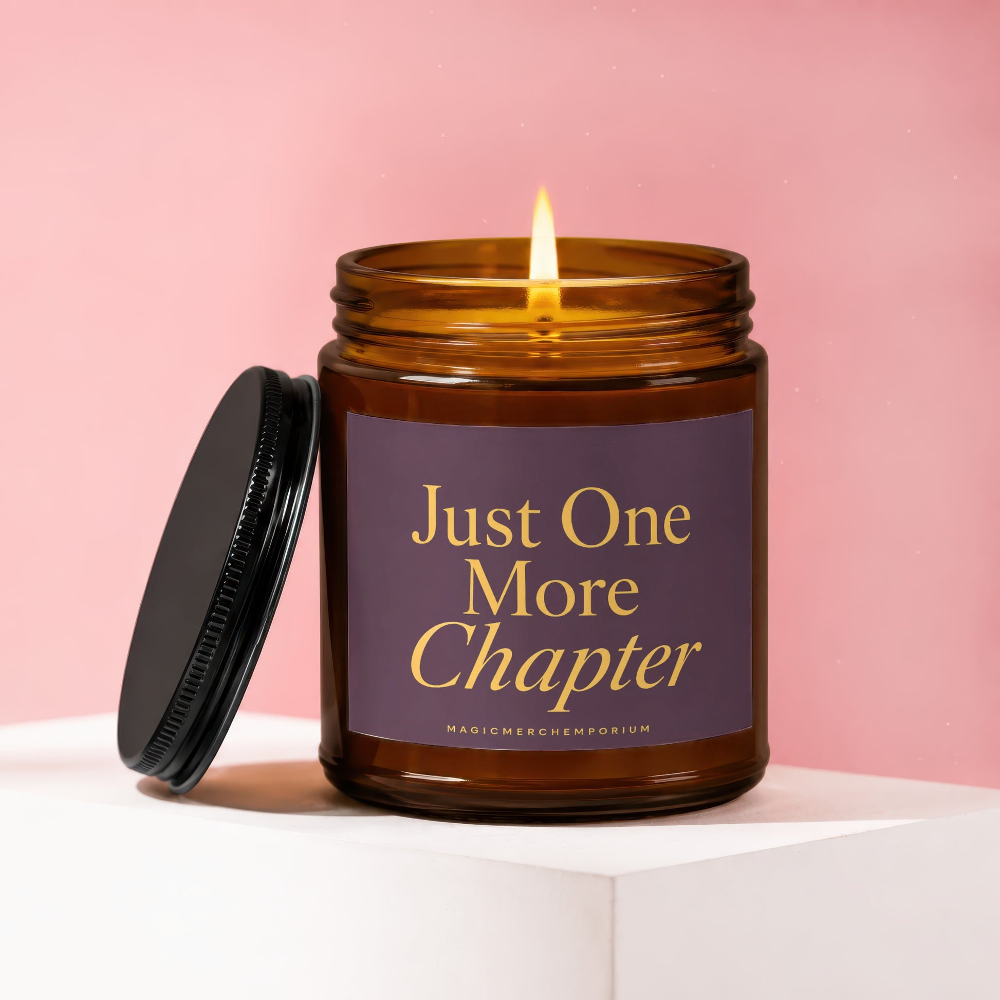 Amber jar candle with lit flame, dark lid, and "Just One More Chapter" label.