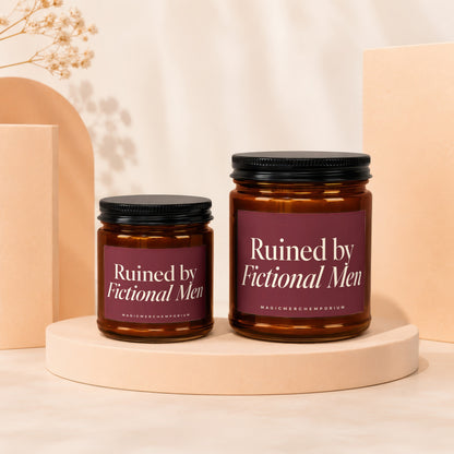 Two amber glass candles with black lids and maroon labels that read "Ruined by Fictional Men."