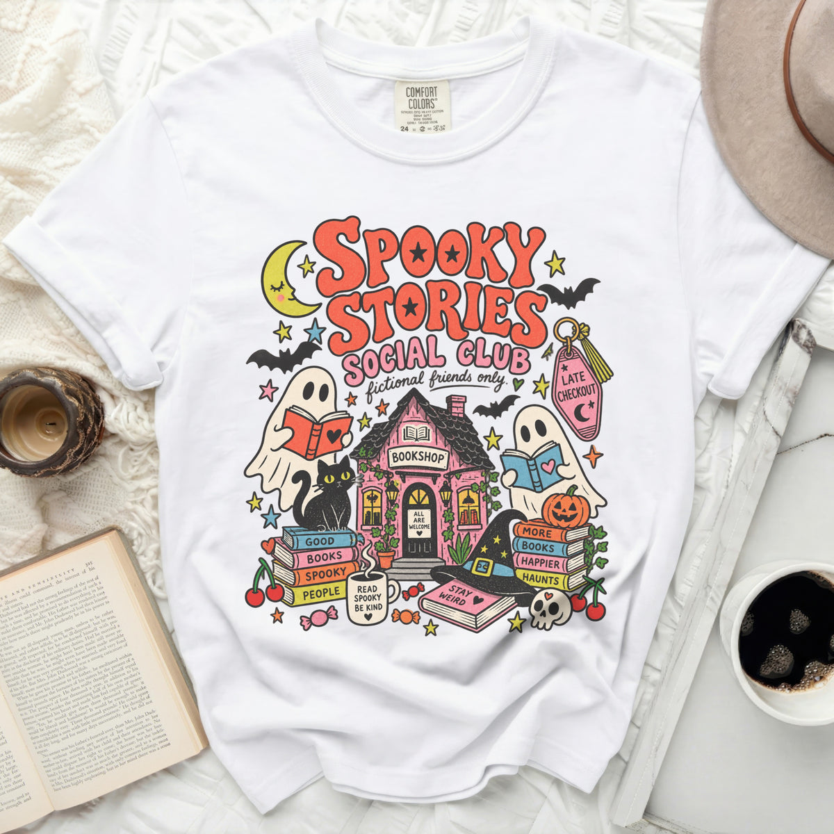White t-shirt with a "Spooky Stories Social Club" graphic featuring ghosts, books, and a bookshop.