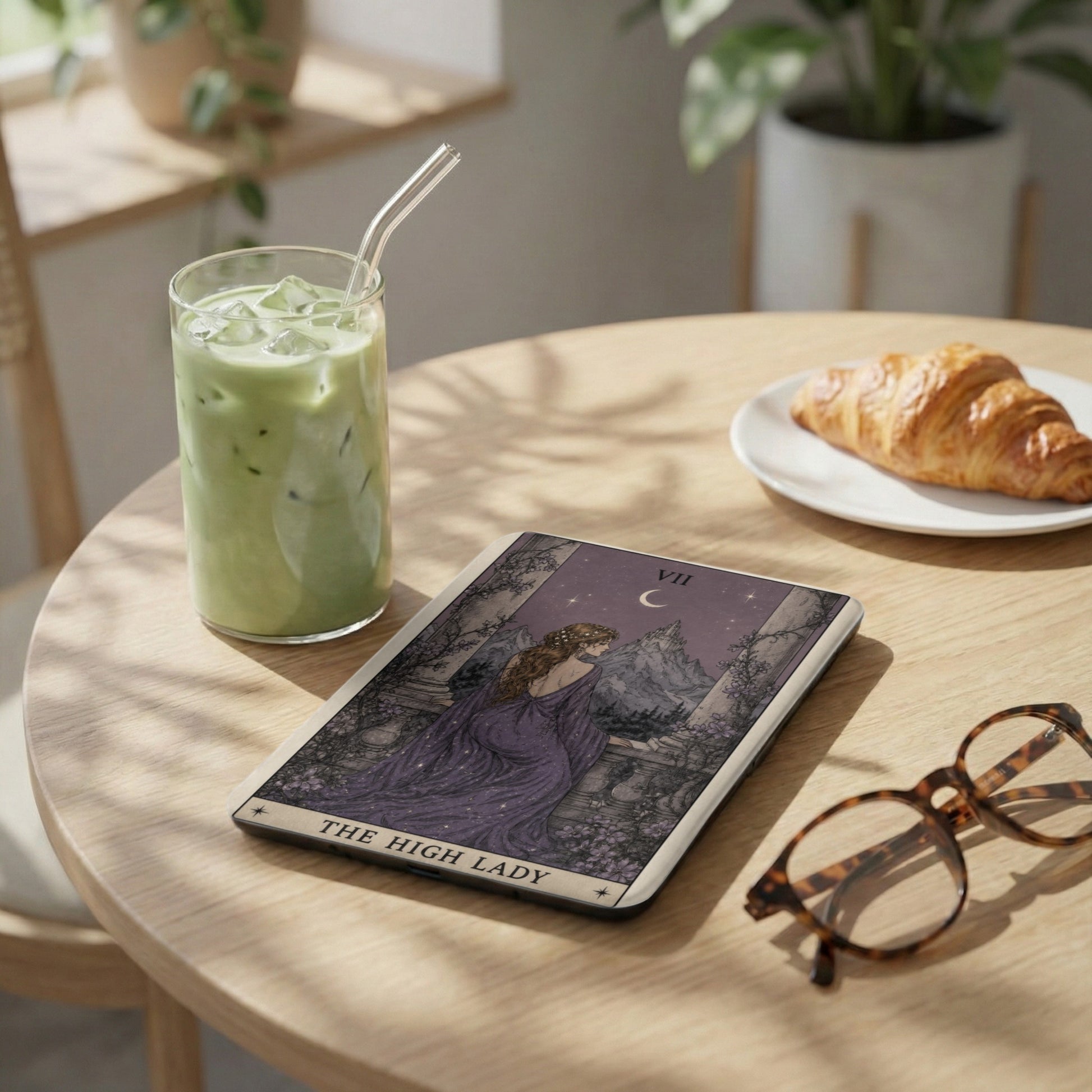 Tarot card "The High Lady" with a woman in a purple dress, beside a matcha drink and croissant.