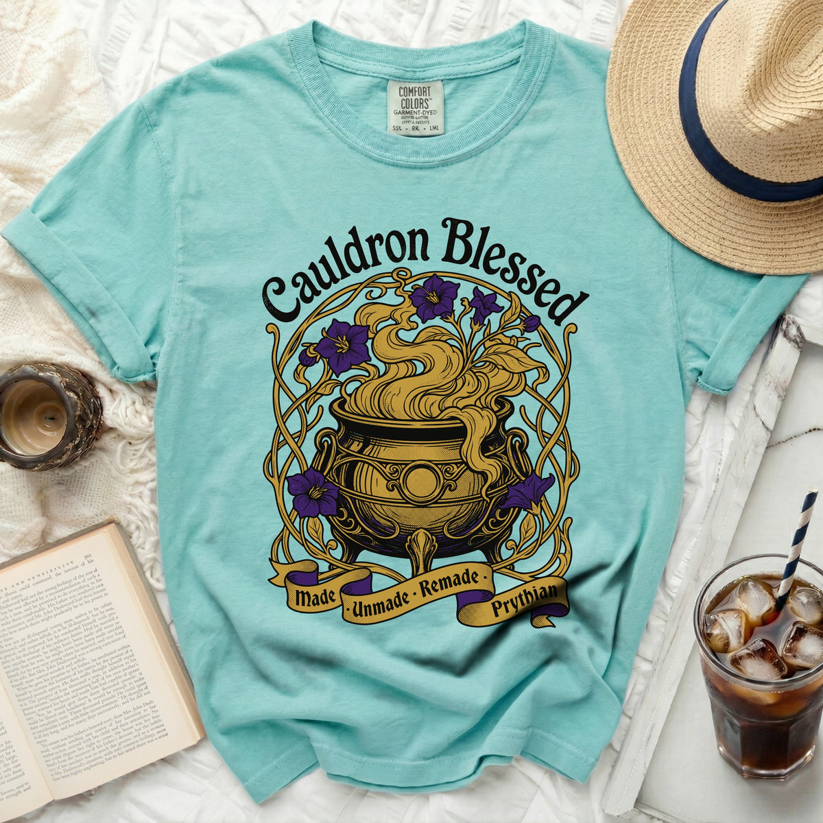 Teal t-shirt with "Cauldron Blessed" graphic, purple flowers, and witchy cauldron.