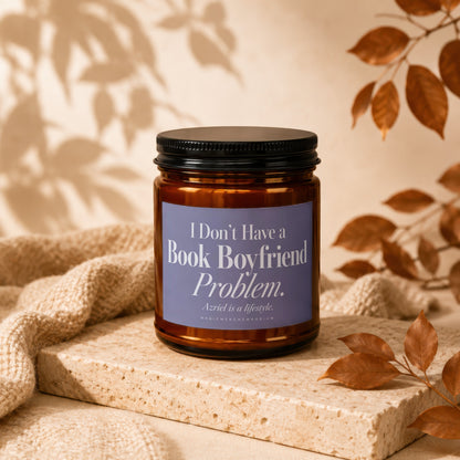 An amber jar candle with a purple label resting on a stone platform with autumn leaves.