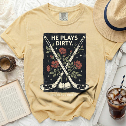 Yellow t-shirt with hockey sticks, flowers, and text "HE PLAYS DIRTY. SHE READS DIRTIER."