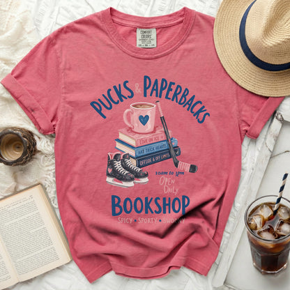 Pink t-shirt with "Pucks & Paperbacks" bookshop graphic.