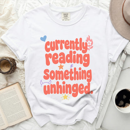White t-shirt with orange text "currently reading something unhinged"