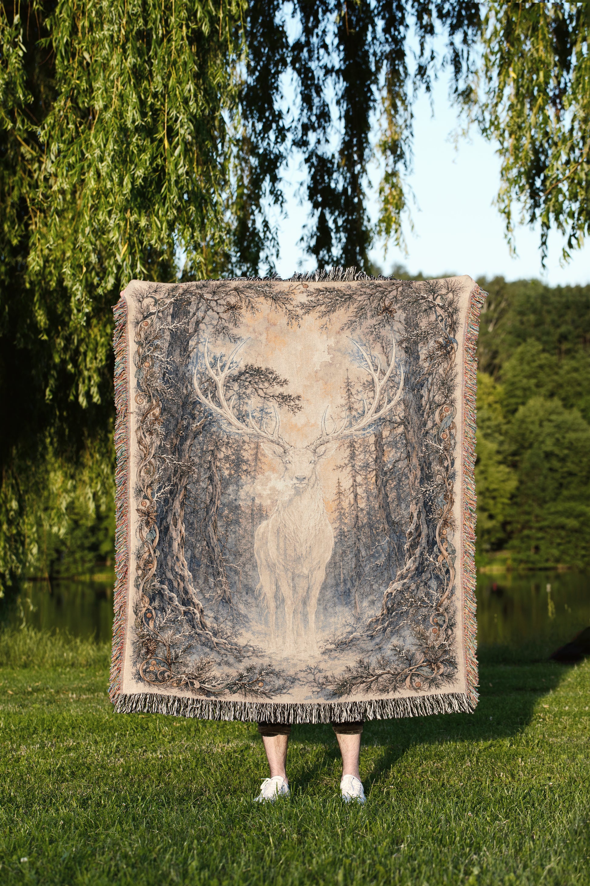 A person is standing in a grassy area, holding a large square blanket with a deer image on it.