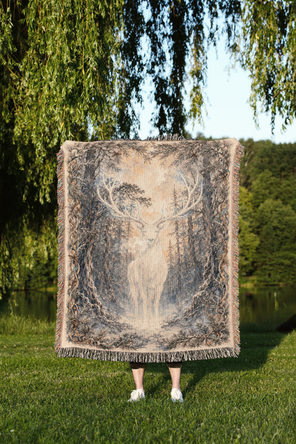 A person is standing in a grassy area, holding a large square blanket with a deer image on it.