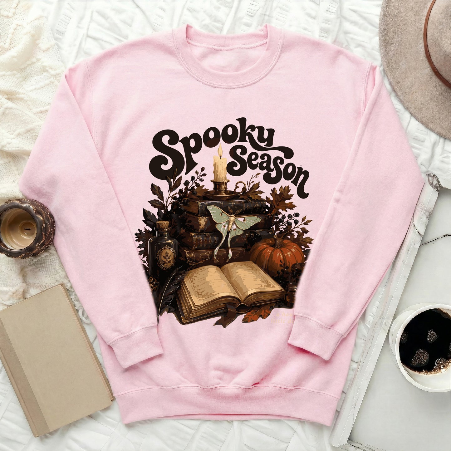 Pink sweatshirt with "Spooky Season" graphic featuring books, candle, moth, and pumpkin.