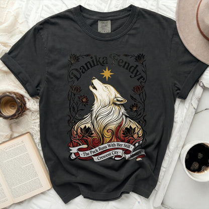 Dark t-shirt with a howling wolf graphic, "Danika Fendyra," and "The Pack Runs With Her Still - Crescent City - Always."