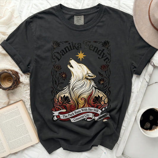 Dark t-shirt with a howling wolf graphic, "Danika Fendyra," and "The Pack Runs With Her Still - Crescent City - Always."