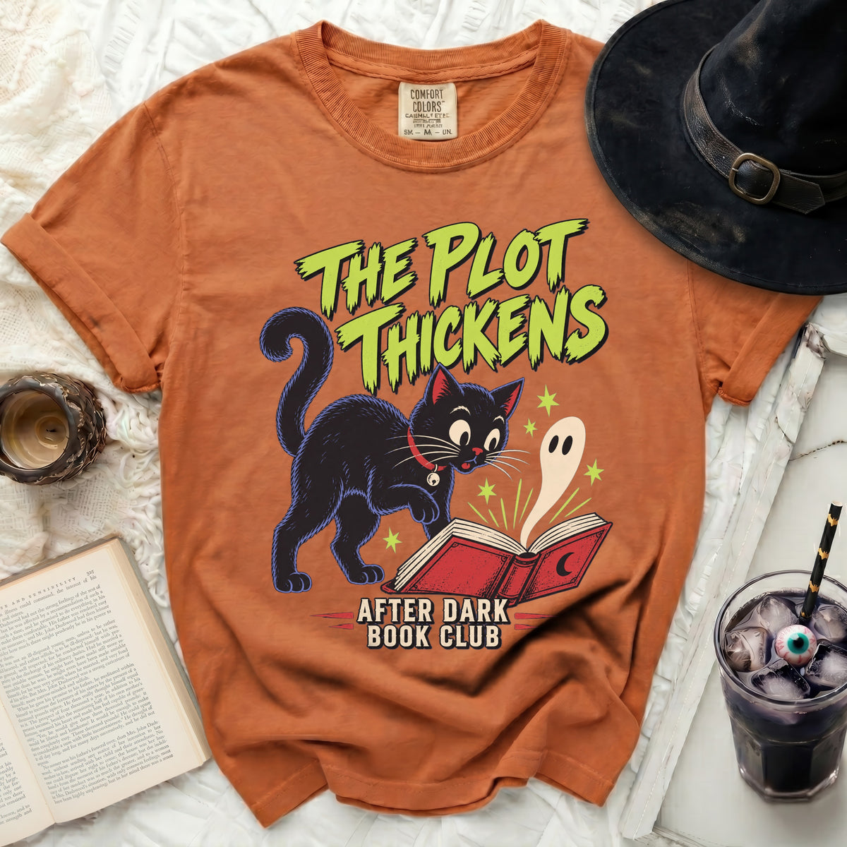 Orange t-shirt with graphic of black cat, ghost, and text "The Plot Thickens After Dark Book Club".