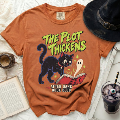 Orange t-shirt with graphic of black cat, ghost, and text "The Plot Thickens After Dark Book Club".