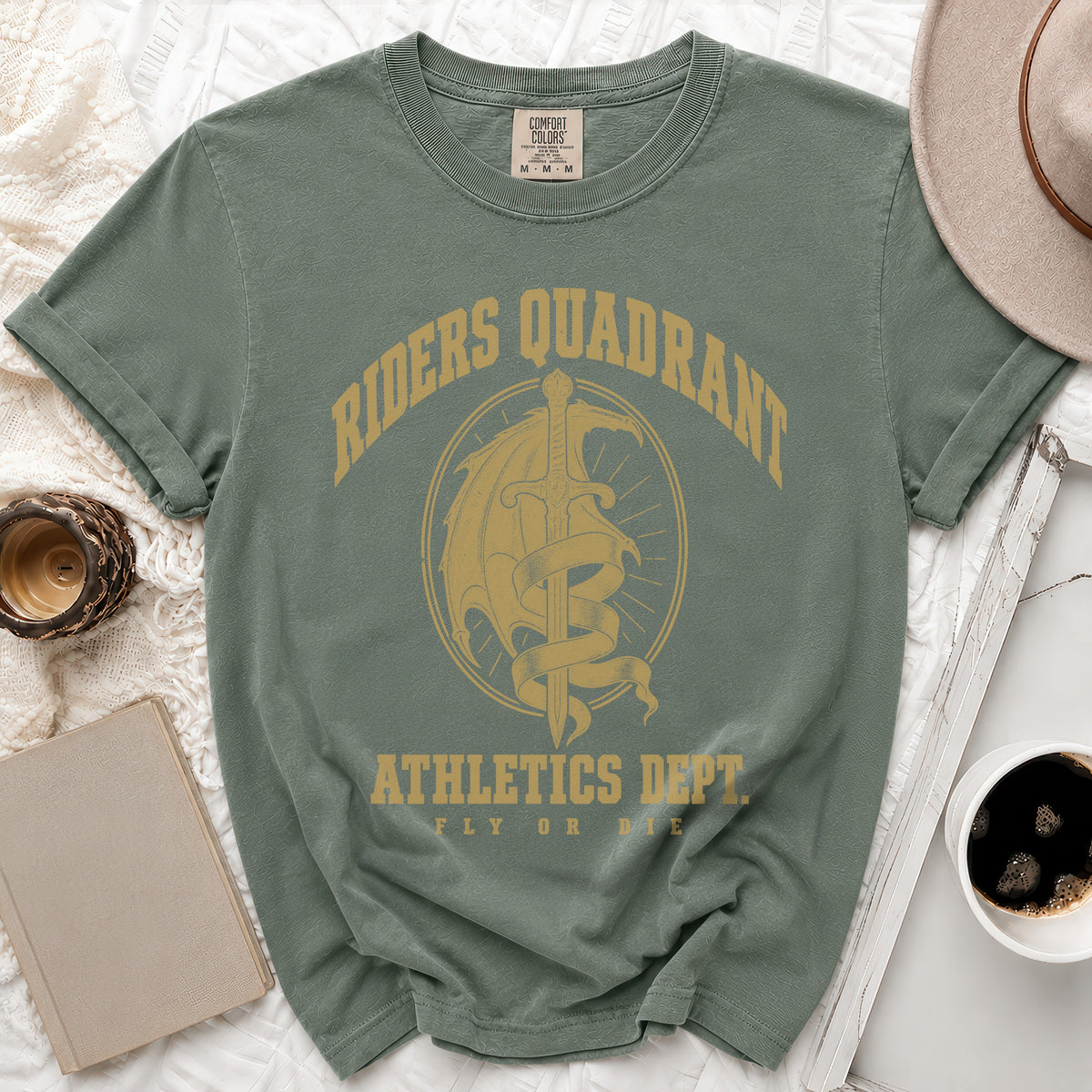 A sage green t-shirt with gold graphic text reading "Riders Quadrant Athletics Dept Fly Or Die".